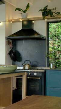 Vertical video: Swinging hanging pans swaying on hooks from breeze in home kitchen, kettle on stove