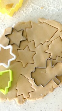 Vertical video: Pressing metal plastic cutters into rolled cookie dough on speckled counter to bake