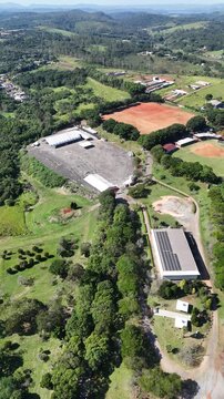 Imagem de drone mostra o Bunkyo de Mogi das Cruzes, SP, com campos, quadras, galp&otilde;es, vegeta&ccedil;&atilde;o e casas pr&oacute;ximas, destacando lazer, esporte e cultura no Alto Tiet&ecirc;.