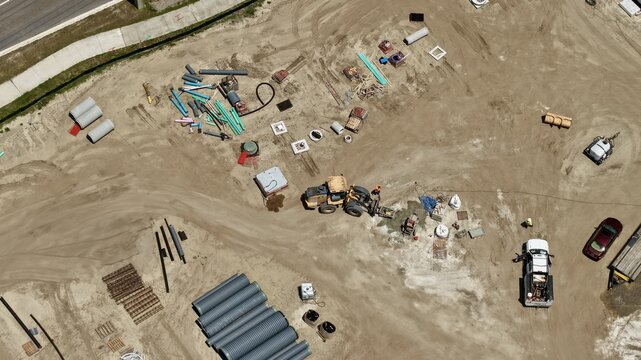 Aerial view of the construction site at Foundry Lane featuring heavy machinery, large drainage pipes, and workers on the sandy ground in World Golf Village, Florida, United States.