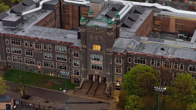 Gloomy high school building in gothic style architecture with illuminated classroom window and entrance, showcasing educational institution exterior in North America