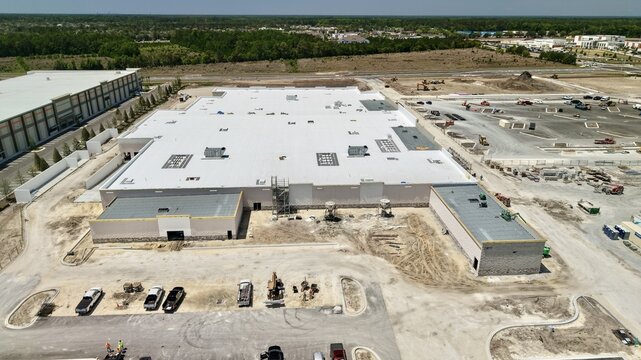 Aerial view of a large commercial building under construction with a white flat roof, surrounding construction site, and heavy machinery World Golf Village, Florida, United States.