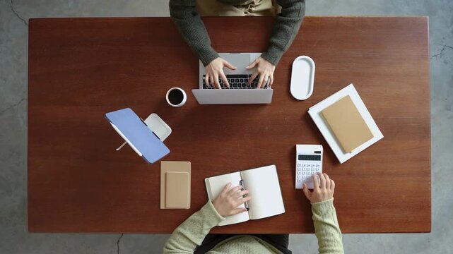Overhead view of person working on laptop at wooden desk with office supplies and calculator in 4k footage