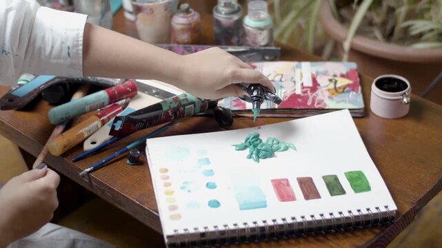 Close-up slow motion watercolor painting on sketchbook with artist hands in natural light