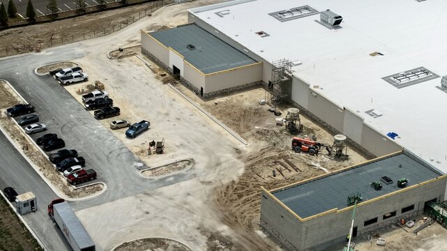 Aerial view of the Foundry Lane construction site featuring a large commercial building with white roofing, machinery, and parked vehicles World Golf Village, Florida, United States.