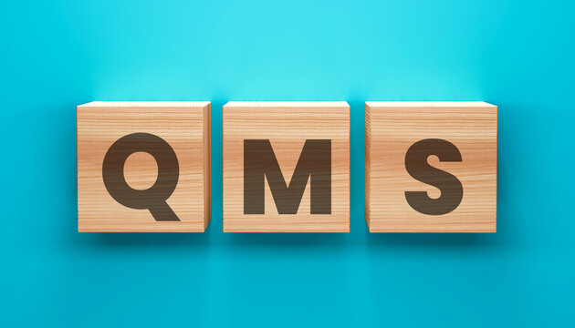 QMS on Cubes: The letters QMS are meticulously arranged on three wooden cubes, symbolizing quality management system. The image presents a clean and modern design for business related topics