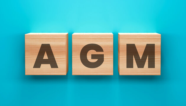 AGM Letter Cubes: Wooden letter cubes spelling AGM arranged neatly against a vibrant blue backdrop, symbolizing Annual General Meeting concept.