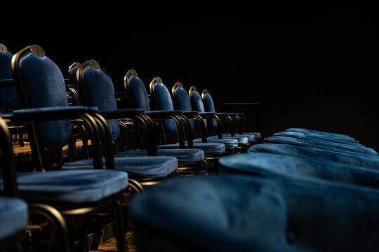 Dimly Lit Cushioned Chairs Near Stage, Closeup Perspective Reveals Upholstery Texture And Worn Comfort, Hush Of Rehearsal And Intimate Cinematic Mood