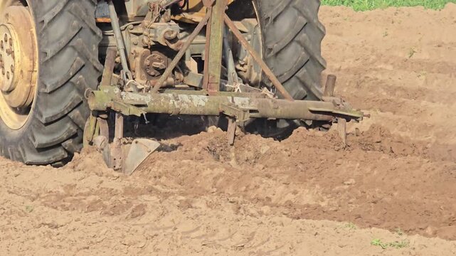 Old tractor with a metal plow cultivating dry soil on a farm during spring field work, traditional agriculture machinery preparing land for planting crops.