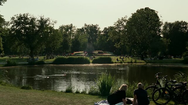 People enjoying a sunny day, relaxing and sunbathing by the pond in Vondelpark, Amsterdam