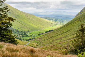 Obraz premium Glengesh Pass winding through a green mountain valley in County Donegal, Ireland. A scenic road landscape of the Wild Atlantic Way and remote Irish highlands.