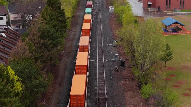 Aerial freight train transporting containers on railway tracks through suburbs showcasing industrial import and export logistics and supply chain systems in North America