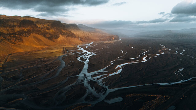 Aerial view of Lomagnupur mountain and the intricate braided glacial river channels flowing through dark volcanic plains in Skaftarhreppur, Iceland.