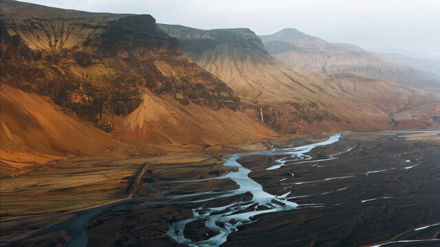 Aerial view of the massive Lomagnupur mountain and a winding braided river flowing through the volcanic landscape in Skaftarhreppur, Iceland.