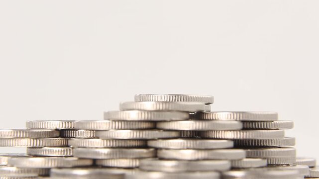 Large flat pile of silver coins spread widely across surface on light gray background in seamless loop, static composition conveying abundance, savings and financial wealth concept. Looped video