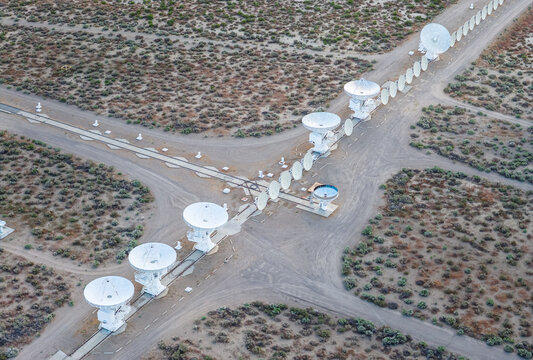 Aerial view of the radio telescope array with large white satellite dishes arranged on tracks in the arid desert landscape of Inyo County, California, United States.