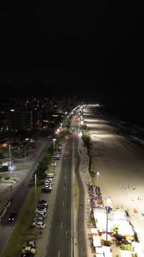Heavy urban traffic flows through the streets of Barra da Tijuca at night, with bright car lights and blurry lines of movement along the highway