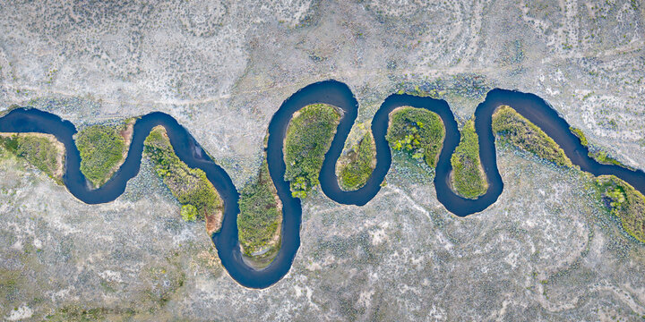 Aerial view of the meandering Owens River flowing through an arid landscape with lush green vegetation along the banks in Inyo County, California, United States.