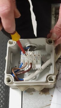 Electrical service engineer inspecting wiring inside a junction box and testing circuits for continuity and voltage during maintenance and fault diagnosis