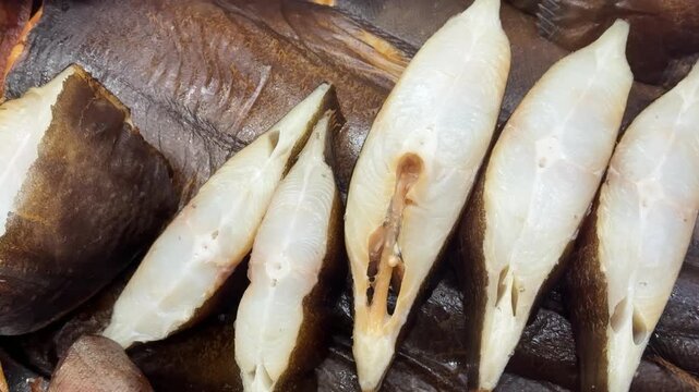 Cold smoked halibut steaks on counter, close-up of glistening white flesh and brown skin on chilled tray, market display suggests