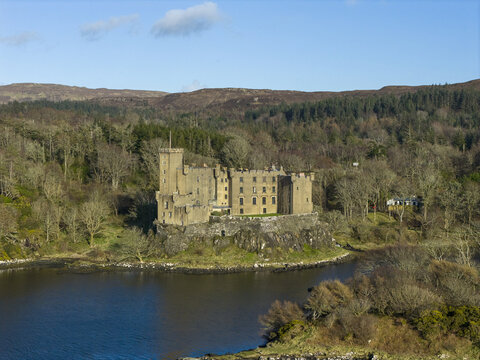 Aerial view of Dunvegan Castle and Gardens situated on a rocky outcrop overlooking the water and surrounded by lush forests and rolling hills in Isle of Skye, Scotland, United Kingdom.