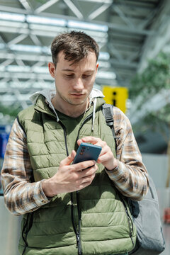 Young male traveler using smartphone while standing in modern airport departure area