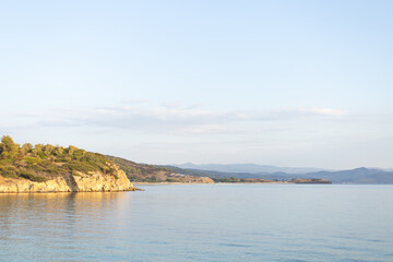 Fototapeta premium Golden hour light on calm Mediterranean sea and rocky coast with hills