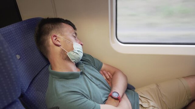 Tired sleeping train commuter wearing PPE face mask for safety. Concept travel during pandemic. Protective medical mask during the trip. Medical respiratory bandage face in transport.