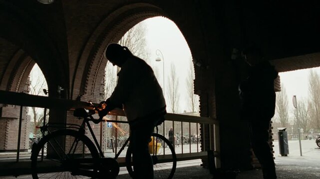 Silhouette of a man using a grinder to saw through a bicycle lock in a city underpass