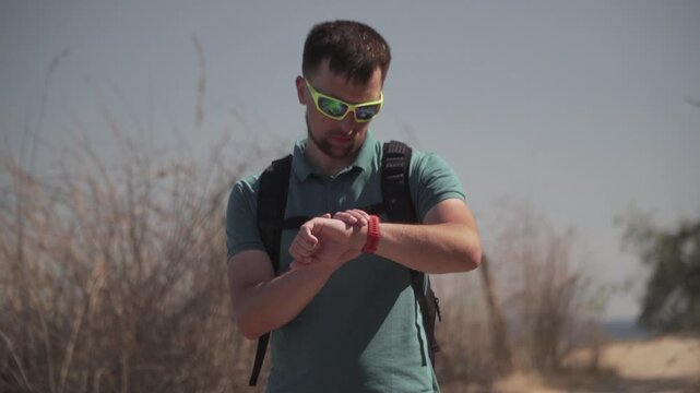 Tourist man in sunglasses checking sports watch with navigation and map, male hiker using modern smartwatch with GPS route on Lycian Way Turkey or Odessa Ukraine near Black Sea coast.