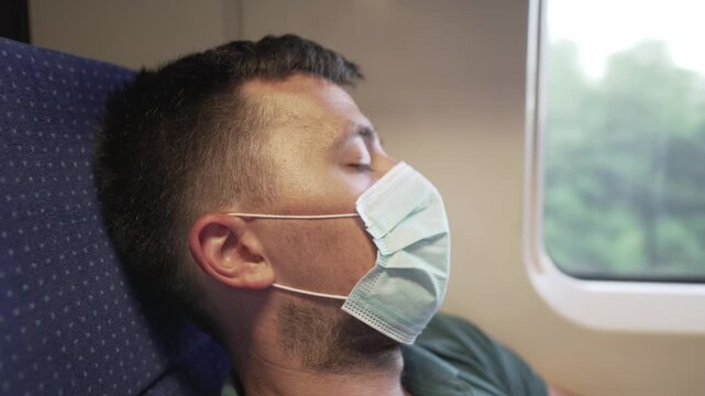 Travel safely public transport. Young man in medical mask sleeps near train window. Train passenger in protective mask on face resting. New normal travel concept. Commuter sleep covid 19, coronavirus.