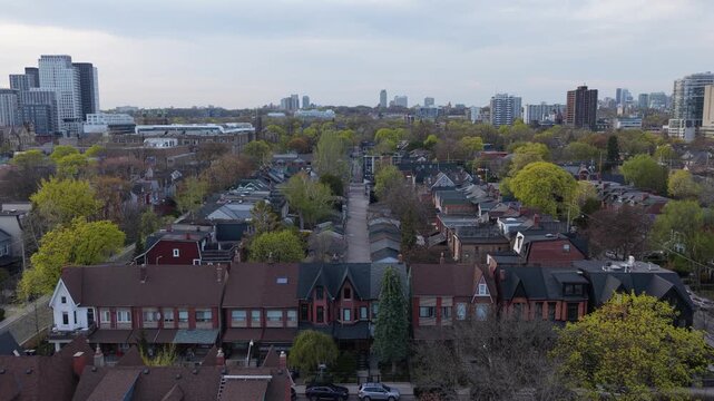 Aerial perspective of residential houses and green trees in a North American neighborhood during springtime, with modern skyscrapers on distant cityscape horizon