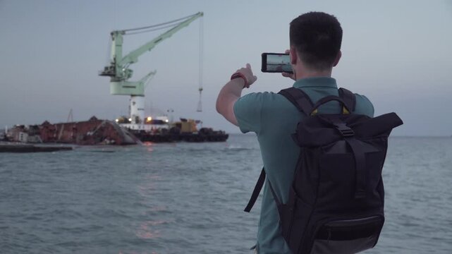 Man blogger records video blog on mobile phone for social media about accident of wreck tanker Delfi with oil in Odessa. Journalist reports on pollution of sea with oil products. Ecology problems.