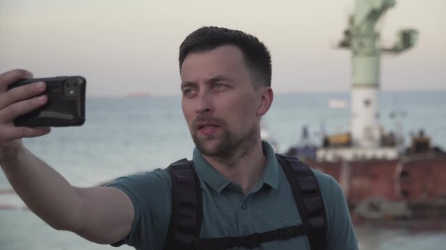 Man blogger records video blog on mobile phone for social media about accident of wreck tanker Delfi with oil in Odessa. Journalist reports on pollution of sea with oil products. Ecology problems.