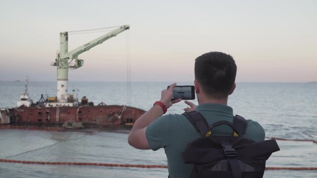 Male blogger is broadcasting live on social networks on journey near sunken tanker Delfi near Odessa. Black Sea coast. Man creating video blog content using smartphone camera about ship accident.