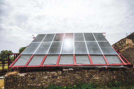 Large photovoltaic roof on red timber frame rises above an old stone ruin, blending clean energy technology with rustic contemporary rural architecture