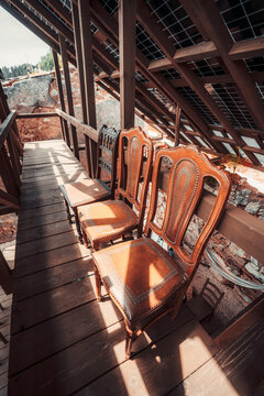 Antique wooden chairs sit on a sunlit timber walkway beneath photovoltaic roof panels, mixing rustic furniture, renewable energy, and rural architecture