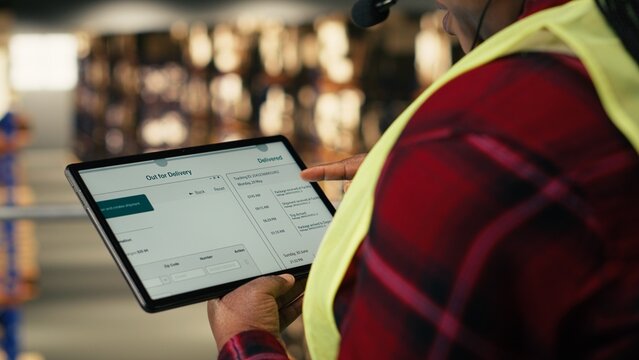 Customer support agent, managing calls, shipment details, cargo tracking, delivery status, warehouse logistics operations while she wears safety vest and headset. Airway bills in industrial space.