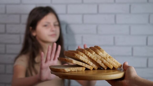 Girl refusing bread on a gluten-free diet. Young girl with celiac disease making a stop gesture with her hands to refuse a plate of bread, demonstrating her commitment to a strict gluten-free diets