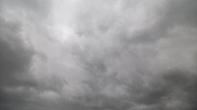 Moody sky with rolling clouds. Dark storm clouds slowly shift under overcast heavens. Gloomy atmospheric scene featuring swirling storm clouds and gentle light punctuations