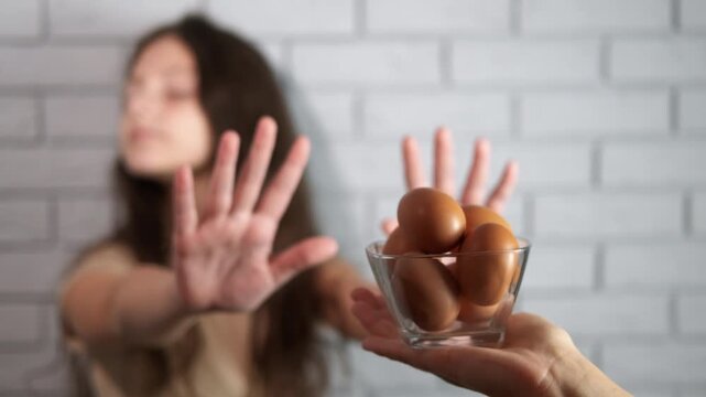 Girl showing allergy symptoms refusing eggs. Unhappy young girl with an intolerance making a stop gesture with her hands, refusing to eat a bowl of fresh brown eggs, a common food allergen