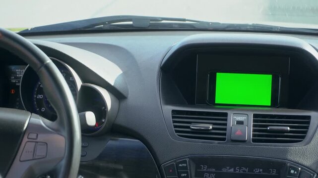 Close-up of a car's dashboard with a smartphone displaying a green screen in the center console display.