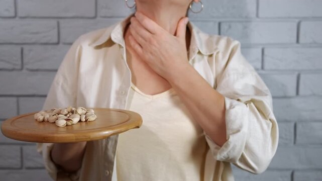 Allergy to pistachios. Unrecognizable woman holding a tray of pistachios and touching her throat, experiencing severe allergic reaction symptoms like difficulty breathing, swelling