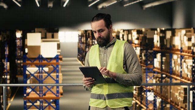 Warehouse employee checking order logistics on tablet in fulfillment center, managing shipment and express delivery details. Man ensuring cargo packages for e-commerce industry, large business.