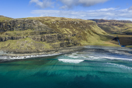 Aerial view of Talisker Bay Beach with turquoise waves crashing against the dark cliffs and rugged hills Isle of Skye, Scotland, United Kingdom.