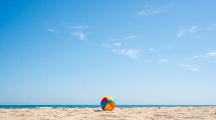 Obraz premium Colorful beach ball resting on sandy shore with ocean and blue sky background