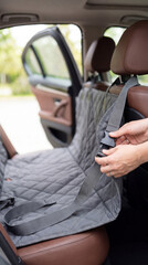 Obraz premium Woman installing protective dog hammock cover on backseat of car. Protective mat for transporting pet in vehicle. Automotive accessory for cleanliness and safety during pet travel trip.