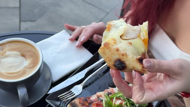 woman bites a slice of pizza salad cherry tomatoes and pizza slices on black square plate gourmet food . plating process with stylish gourmet restaurant atmosphere and appetizing details. 
