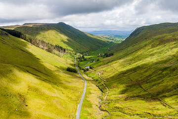 Obraz premium Aerial view of Glengesh Pass curving through a broad green valley in County Donegal, Ireland. A dramatic birds eye landscape of remote mountains and winding roads