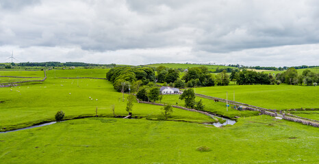 Obraz premium Rolling green meadows with sheep, stone walls and wind turbines near Donegal, Ireland. A rural landscape combining farmland, open scenery and renewable energy.